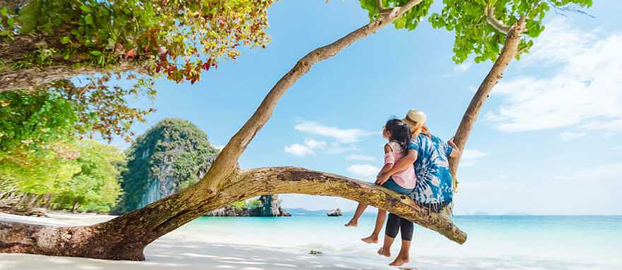 Phuket, Thailand Mother and daughter sitting on a low tree branch on a beach in Phuket, Thailand
