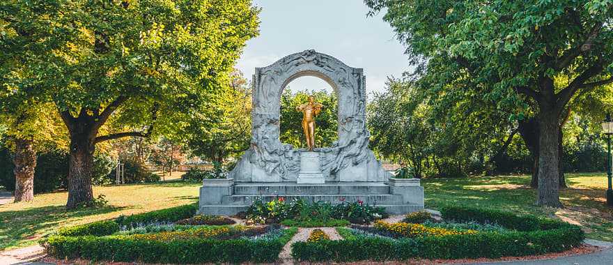 Golden Johann Strauss statue in Stadtpark, Vienna, surrounded by trees and a beautiful garden setting