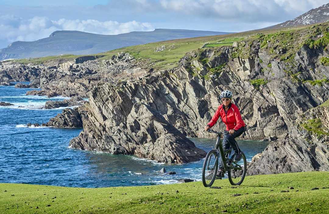 The Cliffs of Croaghaun in County Mayo, Ireland Senior cyclist biking along scenic Irish coastal cliffs with blue ocean waves and rugged landscapes