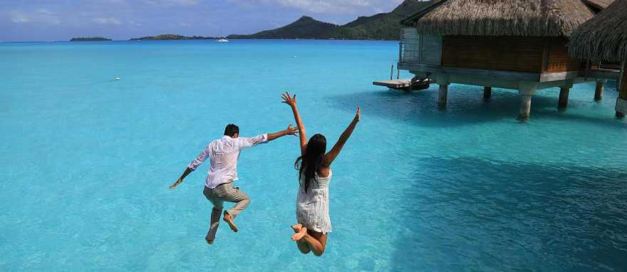 Happy young couple jump into the water from their over water bungalow in Bora Bora Happy young couple jump into the water from their over water bungalow in Bora Bora