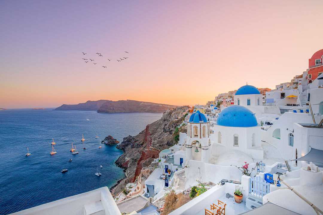 The sun sets over Oia’s blue-domed churches and Aegean Sea.